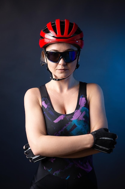 Uma jovem ciclista feminina usando um capacete de segurança e óculos vestidos com um calção posa contra um fundo preto no estúdio