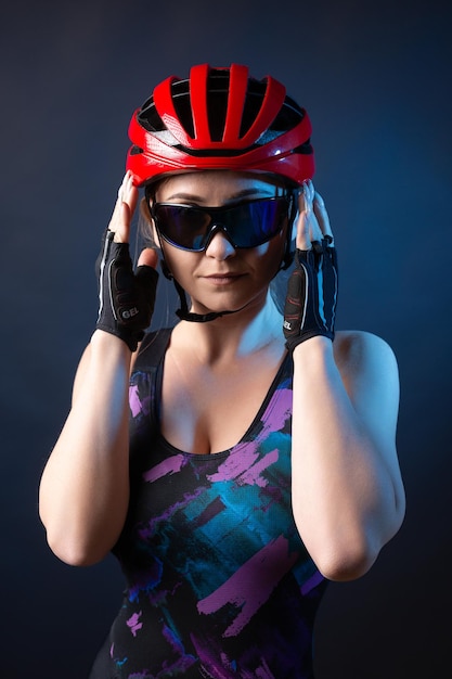 Uma jovem ciclista feminina usando um capacete de segurança e óculos vestidos com um calção posa contra um fundo preto no estúdio