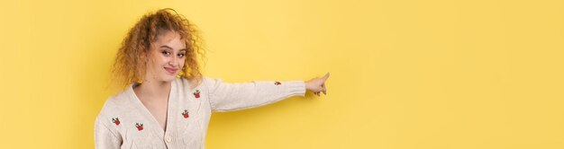 Uma jovem com cabelo encaracolado aponta com um gesto em um fundo de estúdio