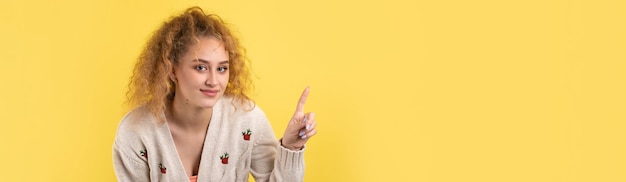 Uma jovem com cabelo encaracolado aponta com um gesto em um fundo de estúdio