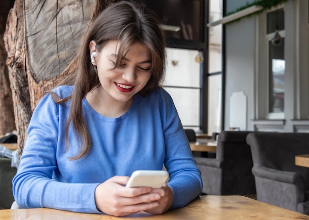 Uma jovem com fones de ouvido sem fio usa o telefone enquanto está sentada em um café