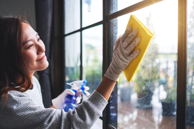 Uma jovem com luva de proteção limpando a janela para o conceito de trabalho doméstico