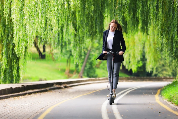 Uma jovem com roupas elegantes anda de scooter elétrica em uma ciclovia