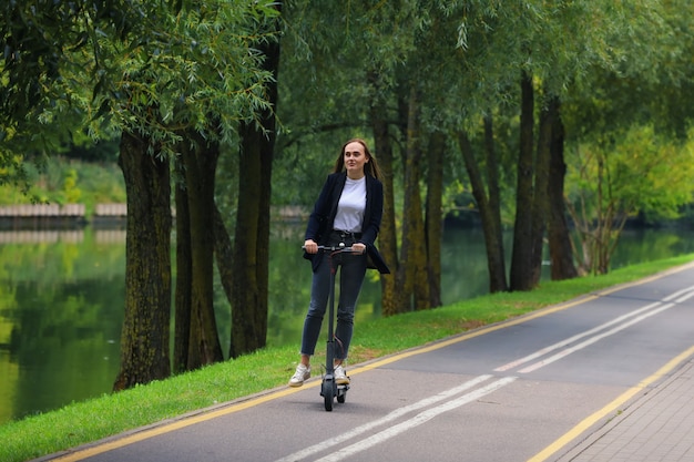 Uma jovem com roupas elegantes anda de scooter elétrica em uma ciclovia