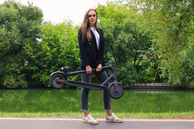 Uma jovem com roupas elegantes posa com uma scooter elétrica no parque