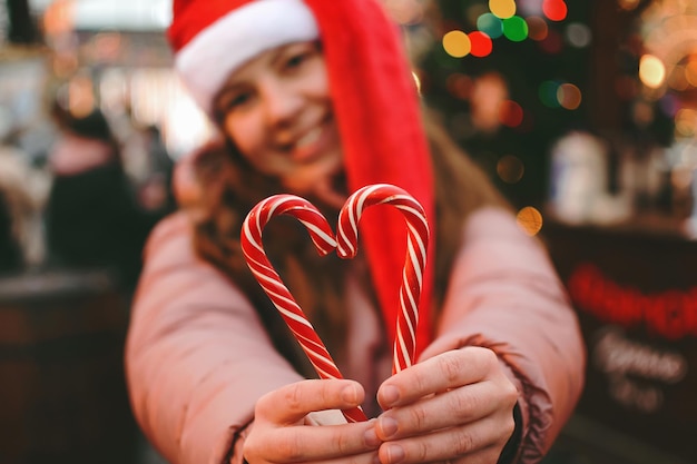 Uma jovem com um chapéu de papai noel mostra um símbolo de coração feito de bastões de doces