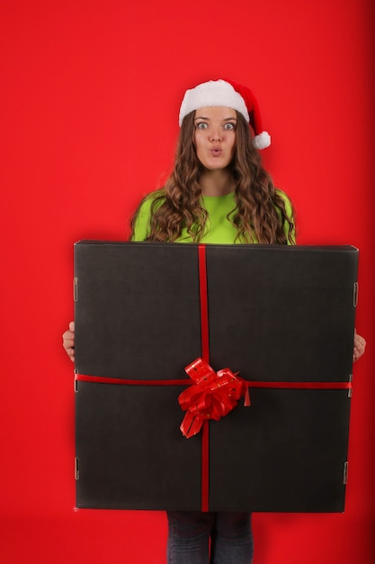 uma jovem com um chapéu de Papai Noel segurando uma grande caixa preta de presente nas mãos