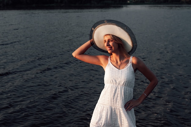 Uma jovem com um chapéu sorri para uma bela loira feliz em um vestido branco de verão está na água ...