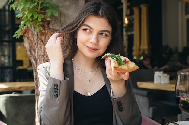 Uma jovem com um copo de vinho e uma fatia de pizza em um restaurante