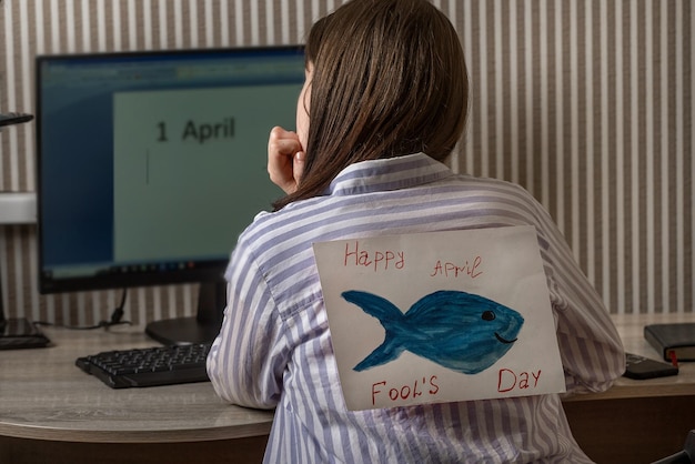Uma jovem com um peixe de papel por trás de dentro de casa trabalha em um computador