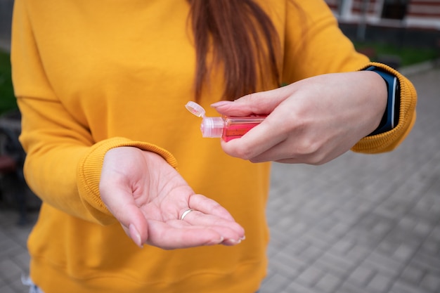 Uma jovem com um suéter amarelo desinfeta as mãos com um anti-séptico