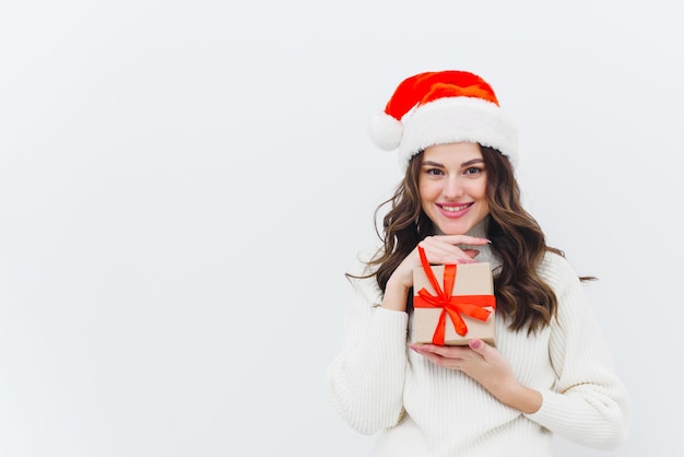 Uma jovem com um suéter branco e um chapéu de Papai Noel segura um presente de Natal em um fundo branco Copiar espaço