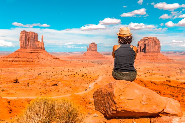 Uma jovem com uma camiseta preta sentada à direita da foto em uma pedra no Monument Valley