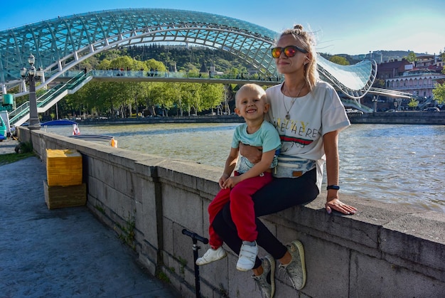 Uma jovem com uma criança no fundo da ponte da paz é uma ponte pedonal arqueada sobre o rio Kura em Tbilisi, capital da Geórgia Tbilisi Geórgia 27 de abril de 2019