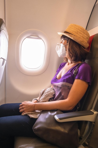 Uma jovem com uma máscara facial dentro de um avião olhando pela janela em voo