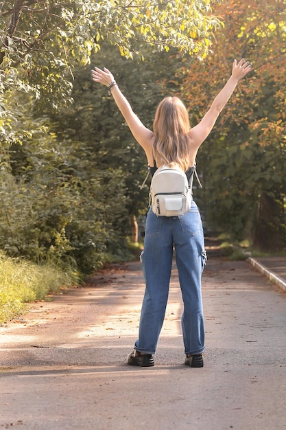 Foto uma jovem com uma mochila branca está em pleno crescimento ao ar livre, duas mãos são levantadas