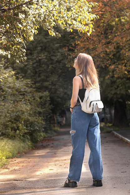 Uma jovem com uma mochila branca fica na rua em pleno crescimento e olha para cima no início do outono