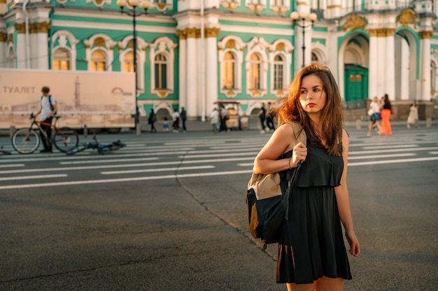 Uma jovem com uma mochila em frente ao palácio de inverno em são petersburgo