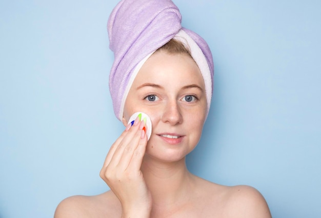 Foto uma jovem com uma toalha na cabeça limpa o rosto com uma almofada de algodão para limpeza facial