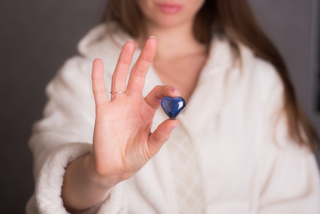 Uma jovem com uma túnica branca tem nas mãos uma pedra de vidro azul na forma de um coração. Pedra preciosa azul grande plana em forma de coração