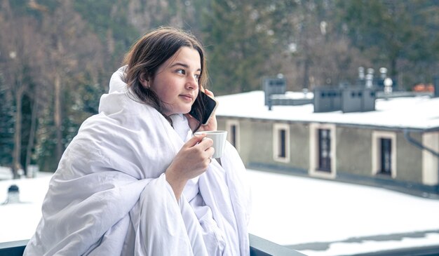 Uma jovem com uma xícara de café na varanda no inverno nas montanhas