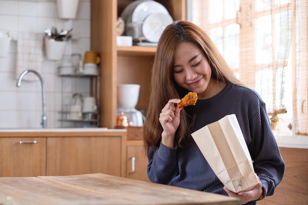 Uma jovem comendo frango frito do saco de papel na cozinha em casa para o conceito de entrega de comida