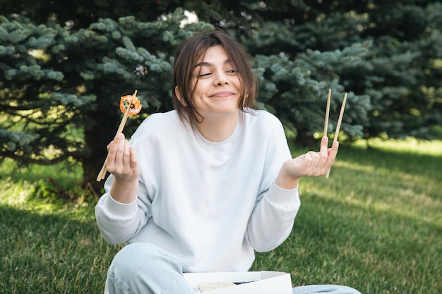 Uma jovem comendo sushi no parque piquenique na natureza