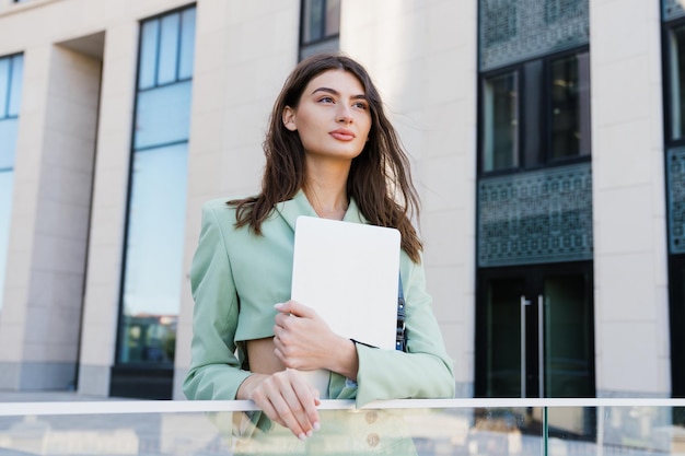 Uma jovem confiante com um laptop posa contra o fundo de edifícios Retrato de negócios do lado de fora