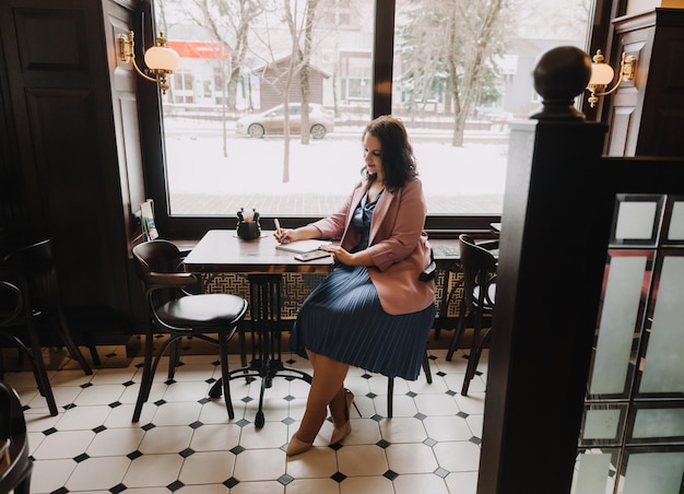 Uma jovem confiante em um terno de negócios trabalha em um laptop enquanto está sentada perto da janela em um caféempresária