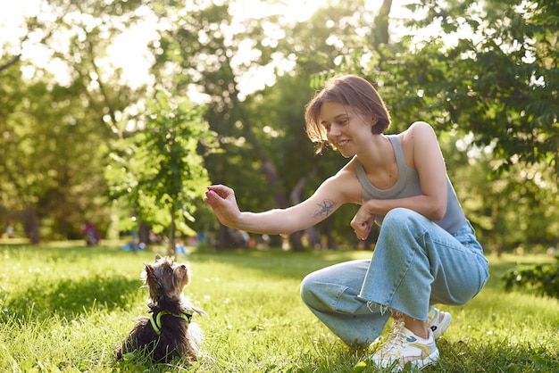 Uma jovem corre e brinca em um parque verde com seu yorkshire terrier.