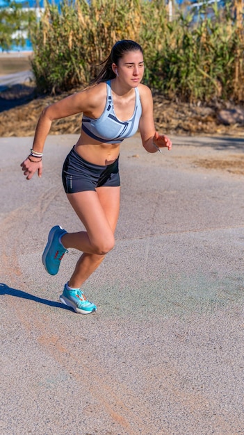 Uma jovem corredora vestida com calças curtas de corrida e um top posicionado com estilo e movimento técnico perfeito com as pernas dobradas e o corpo inclinado pronta para correr em um caminho de asfalto em um parque