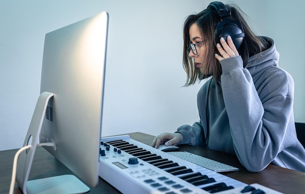 Foto uma jovem cria música usando um teclado musical e um computador