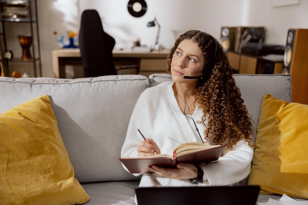 Uma jovem de cabelo encaracolado, vestida com uma camisola branca e uma camiseta branca, senta-se num sofá