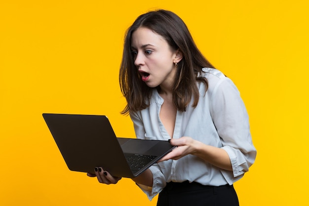 Uma jovem de camisa branca segura um laptop em um fundo amarelo