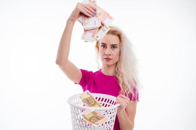 Uma jovem de camiseta rosa joga notas russas no lixo em um fundo branco O conceito de uma economia em queda