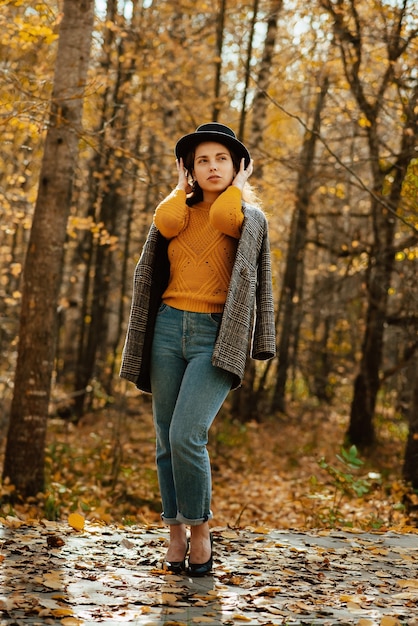 Uma jovem de casaco e chapéu caminha pelo parque de outono
