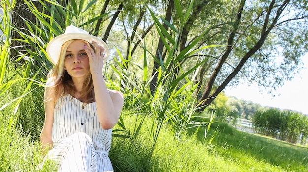uma jovem de chapéu branco está sentada na grama