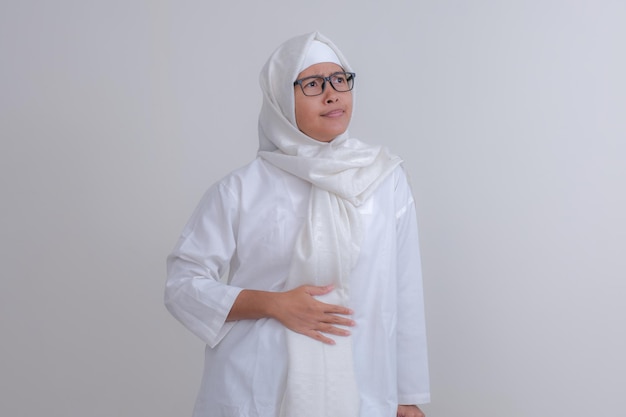 Foto uma jovem de hijab branco está tocando seu estômago