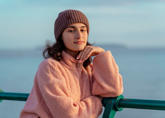 Uma jovem de jeans e uma jaqueta rosa descansando à beira-mar ao pôr do sol