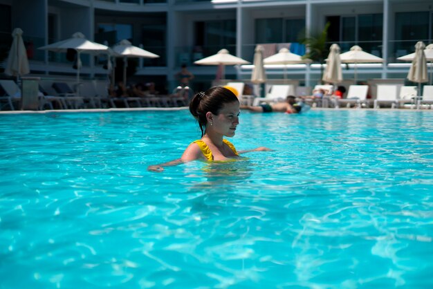 Uma jovem de maiô amarelo nadando na piscina, férias no resort de verão