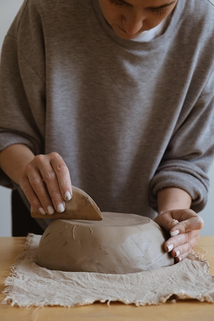 Uma jovem de manga comprida cinza faz um vaso de barro com as próprias mãos em uma oficina de escultura