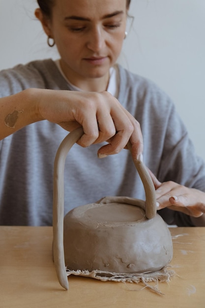 Uma jovem de manga comprida cinza faz um vaso de barro com as próprias mãos em uma oficina de escultura