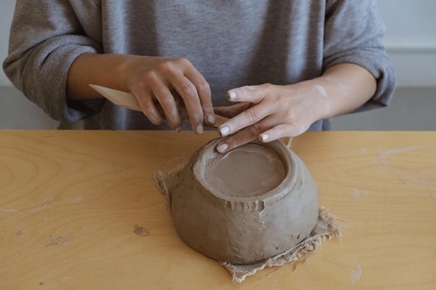 Uma jovem de manga comprida cinza faz um vaso de barro com as próprias mãos em uma oficina de escultura