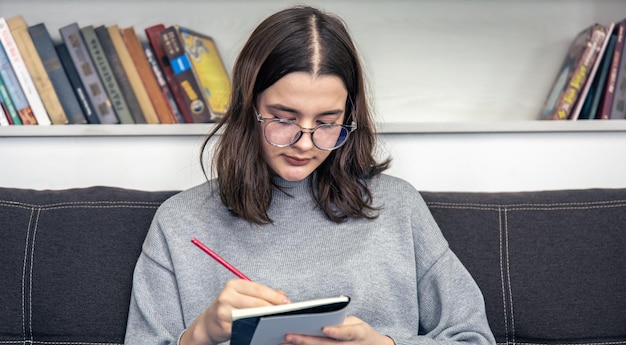 Uma jovem de óculos desenha em um caderno com um lápis