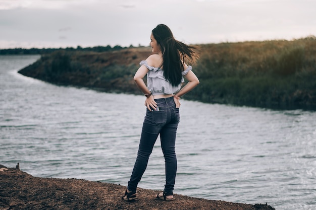 Foto uma jovem de pé volta em um sorriso, uma bela turista mulheres está apreciando o rio e pôr do sol à noite