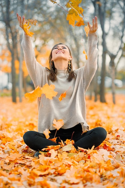 Uma jovem de raça mista feliz sorrindo alegremente joga folhas de outono do lado de fora no espaço de cópia da floresta de outono