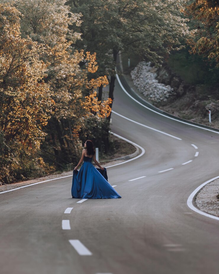 Foto uma jovem de vestido azul a caminhar pela estrada através da floresta.