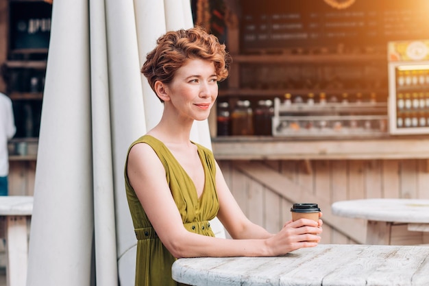 Uma jovem de vestido bebendo café em um café de verão. Mulher bonita com uma xícara de café.