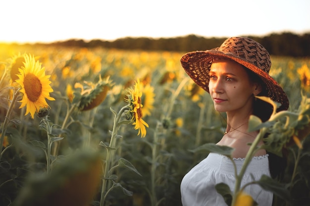 Uma jovem de vestido branco e chapéu em um campo de girassóis ao pôr do sol Retrato de uma mulher com uma figura esbelta em um fundo de flores amarelas