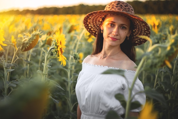 Uma jovem de vestido branco e chapéu em um campo de girassóis ao pôr do sol Retrato de uma mulher com uma figura esbelta em um fundo de flores amarelas